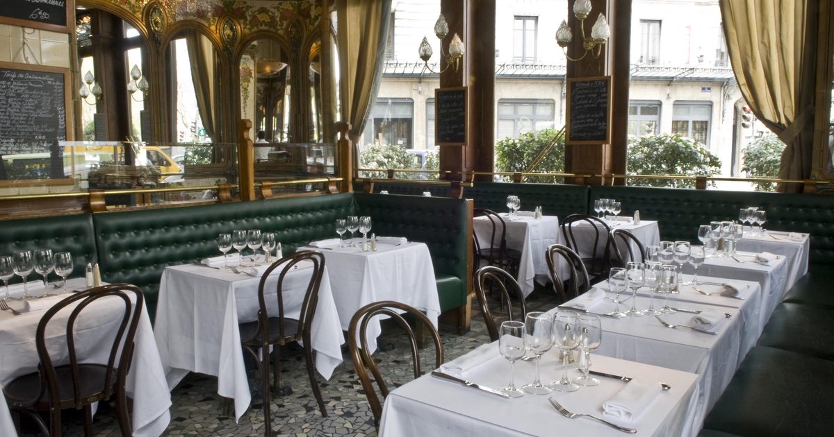 Salle de brasserie avec tables dressées, chaises bistrot et miroirs